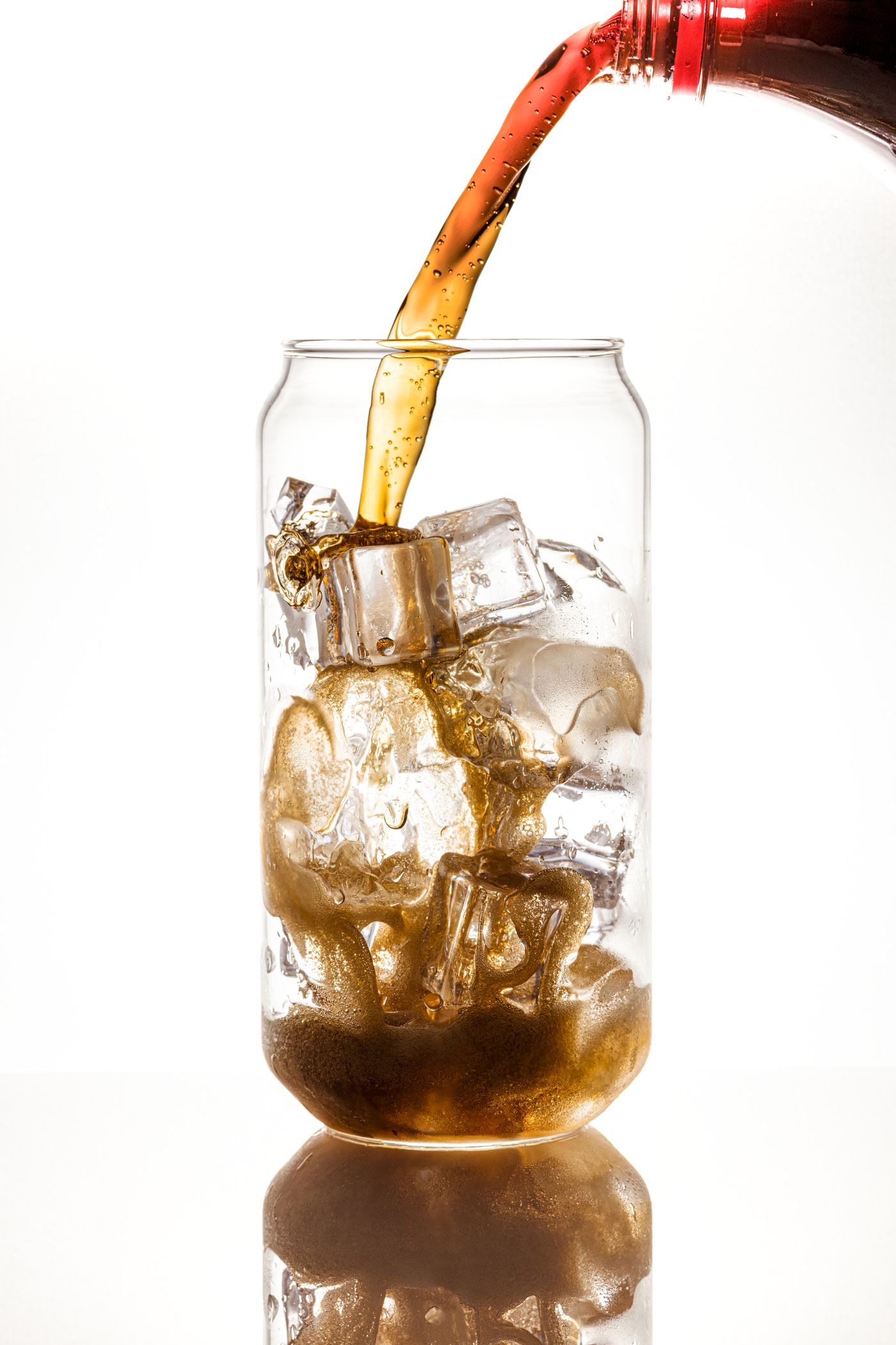 Cold drink being poured over clear ice cubes in a glass